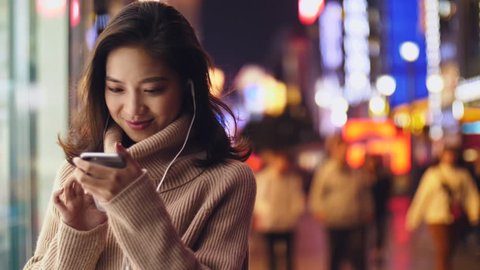 close up of young happy beautiful asian woman using smartphone in the Chengdu street at night 