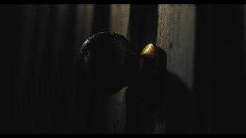 Pushing a door open in a dark, creepy setting. Ghost story, horror, thriller set. Close up on the door knob