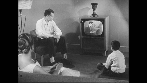 1950s: Family gathered around the TV set in a living room. Hurricane special bulletin plays on TV. Weather man announces hurricane.