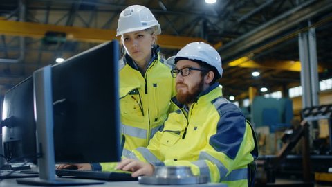 Male Industrial Engineer Works on the Personal Computer while Female Manager Talks about Project. They Work in Heavy Industry Manufacturing Factory. Shot on RED EPIC-W 8K Helium Cinema Camera.