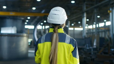 Following Shot of Female Industrial Worker in the Hard Hat Walking Through Heavy Industry Manufacturing Factory. In the Background Various Metalwork Project Parts Lying.  Shot on RED EPIC-W 8K Helium 