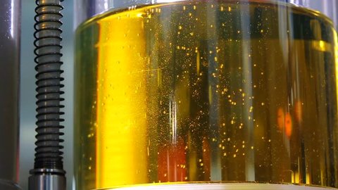 Air small bubbles in yellow engine oil for filter with cellulose, in transparent reservoir, closeup