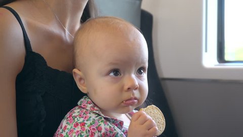 A baby girl eating a flat biscuit on the train. Close-up shot.