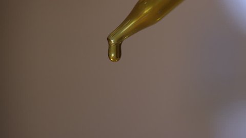 Eyedropper squeezing out yellow-gold droplets, closeup