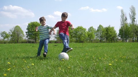 Two boys hit the ball on green play field with dandelions, slow motion 250 fps