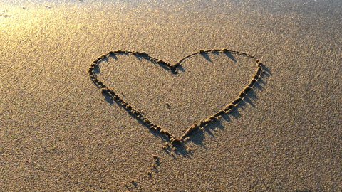 Heart drawn on the beach sand with sea foam and wave 