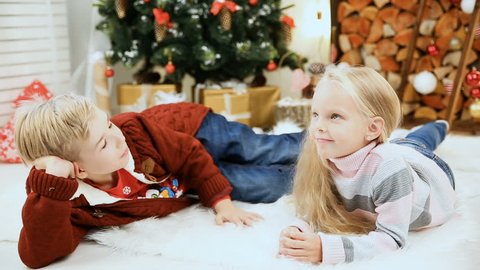 boy and girl posing near Christmas tree indoors