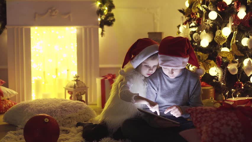 Excited boy and girl sitting near Christmas tree, playing tablet game together.