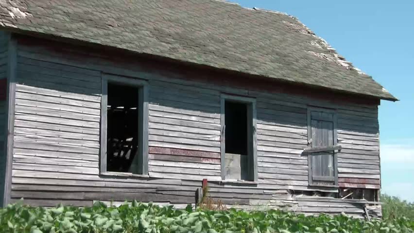 Shirtless man waving to come into old abandoned farmhouse through window without glass.