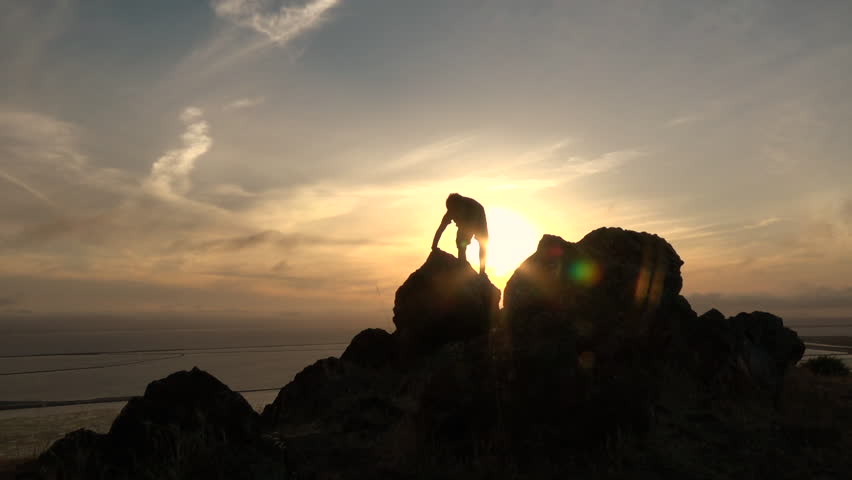 Active boy climbing big rock at sunset