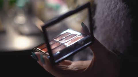 a professional make-up artist girl holds in her hand a pallet with cosmetic means of a shadow for a century lipstick proof-readers. The woman dips the brush in the makeup and applies makeup 