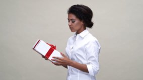 Intrigued african woman in shirt holding gift box over gray background