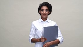 Happy african woman in shirt showing thumb up while holding folder with documents over gray background