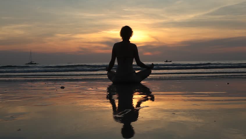Silhouette of a young woman meditating on the beach in the evening