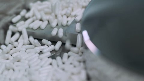 Production of pharmaceuticals and drugs, large number of capsules, white tablets on the conveyor, production line.
