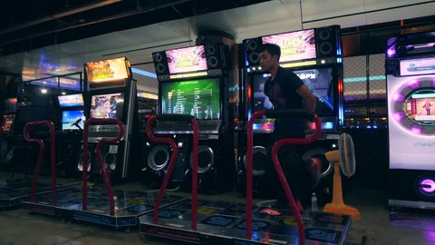 Asian Man Dancing on Dance Revolution Arcade Machine Pad in Game Zone MBK Shopping Center. 4K. Bangkok, Thailand - 15 NOV 2017.