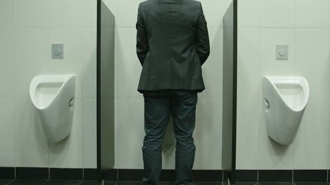 Man peeing to toilet bowl in restroom. Long shot