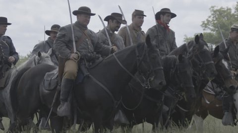VIRGINIA - MAY 2017 - large-scale, epic Civil War anniversary reenactment -- before battle. Confederate Cavalry and officers ride horses across tall grass field with swords, flags and muskets.