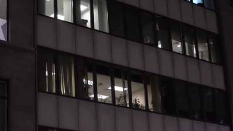 NX Night time establishing shot urban city office or apartment building exterior. Lights on through windows on skyscraper facade. Day / Night matching shot