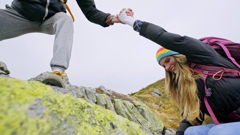 Young woman climbing rocks helped by her boyfriend