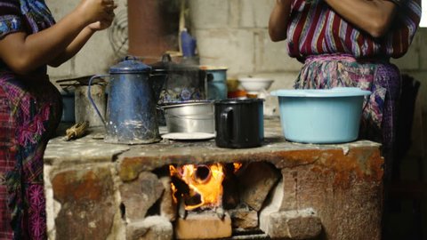 A pair of indigenous women dressed in traditional clothes make tortillas over a firewood kitchen in Guatemala.