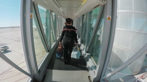 Woman walking in flight connections with baggage in hands. Airpport hub or tunnel to airplane, back view.