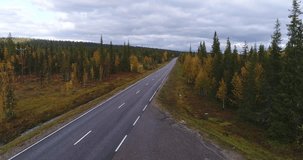 Autumn color road, Cinema 4k aerial view of a grey car driving on a fall road, between colorful autumn forest and tunturi fjeld mountains, on a rainy day,Lapland, Finland