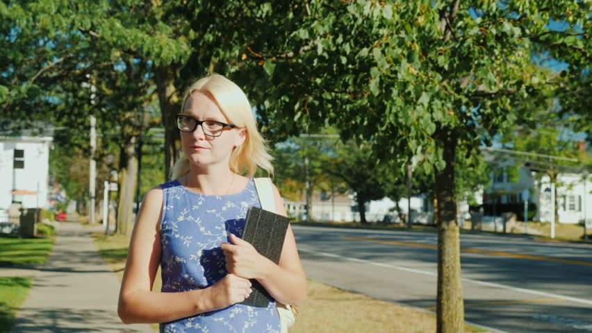 A woman walks leisurely along the street of a small suburban city in the United States. In his hand carries a tablet. Steadicam shot