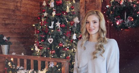 Snowflakes flying down slowly. A beautiful young blonde girl in a warm sweater warms her hands with her breath. It's cold outside. Celebrating Christmas and New Year.