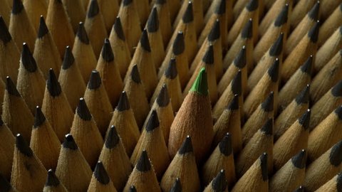 Identical graphite pencils in rotation and one green crayon. Close up of bunch of identical sharp graphite pencils in rotation and one different, unique green crayon that stands out. Studio shot.