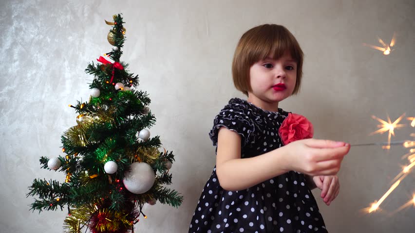 Young german girl celebrates Christmas holding Bengali flame. Child is dressed in smart black dress with polka dots with pink brooch and bright make-up. Girl amazed to watch the sparks of fire next to