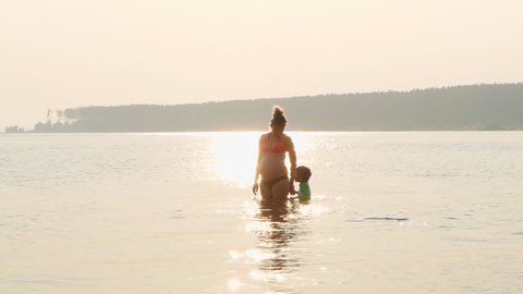 Pregnant mother and child are swimming in sea at sunset