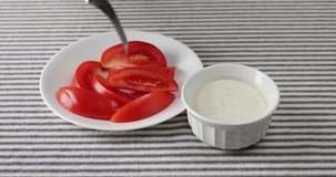 A white plate with several sections of roma tomatoes with one slice being selected with a fork and dipped into a bowl of ranch dressing only for the section to fall into the bowl.
