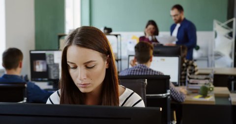 Close up of of young beautiful woman working thoughtfully on the computer in the modern office space. Office workers on the background. Portrait shot