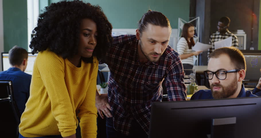Young succesful team working and discussing a business project at the computer. Multi-ethnic male and female workers in the urban office.