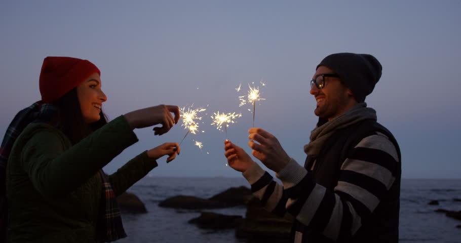 Young attractive couple laughing and playing with sparklers on twilight at the rocky seacoast. Outside