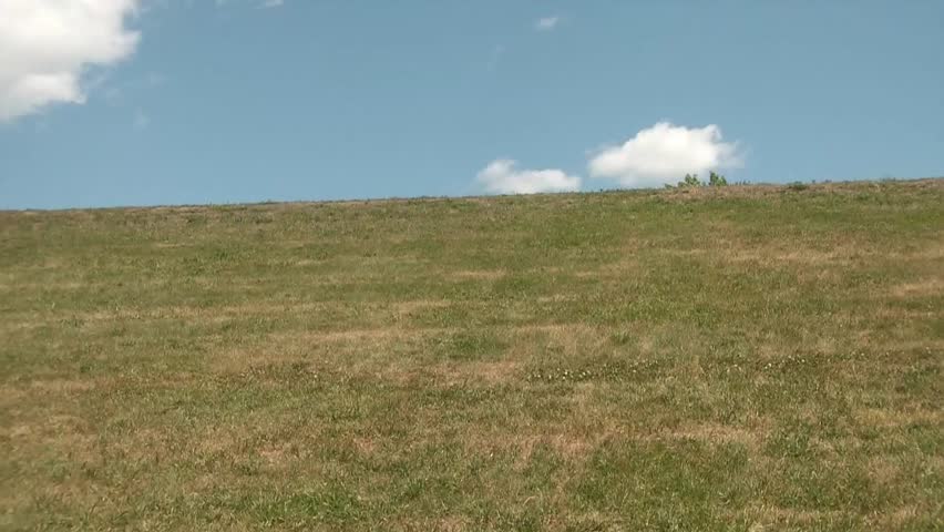 Guy exercising by running up hill towards clouds and blue sky, and then running down to camera.