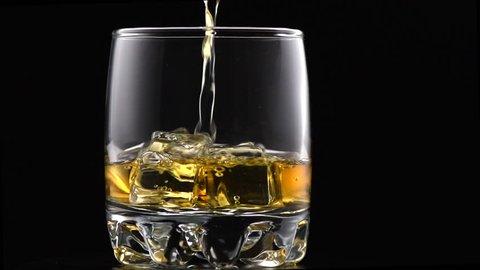 Whiskey with ice. Pouring whisky from the bottle on black background. Glass of rum alcohol close-up. Isolated on black. 4K UHD video