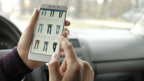 A man looks at the goods in the online clothing store, sitting in the car. Smart phone online shopping.