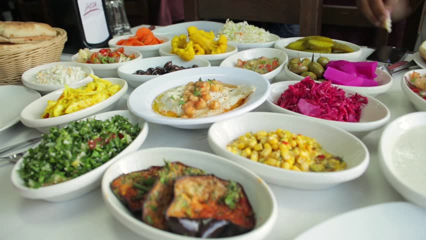 Middle east food plates and dishes. Arrangement of arabic food specialties on a table. Vegetables like olives or carrots but also tabouleh and fried eggplant. Two hands take a dip into the hummus. | Shutterstock HD Video #32873509