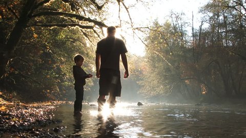 Beautiful slow motion of father and son together at the river having fun skipping rocks on sunny fall day in Washington.