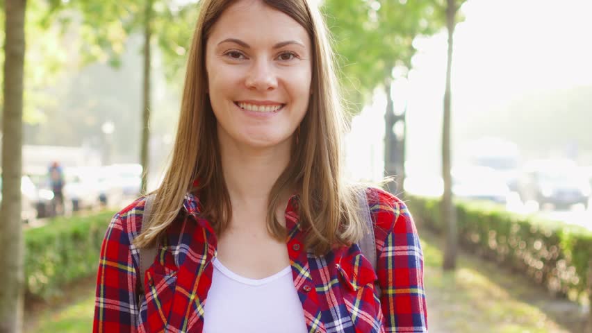 Portrait of happy cheerful young woman enjoying nature. Walking in green autumn park smiling at camera