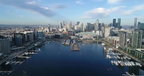 Aerial flying towards waterfront on Yarra river in Docklands suburb of Melbourne with view of city CBD towers.
