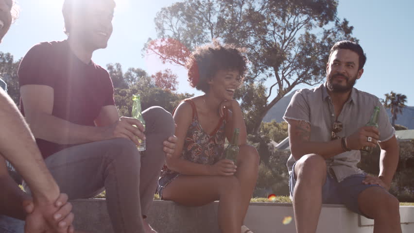 Group of friends sitting together with beers and talking. Happy men and woman having a party outdoors on a summer day.