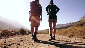 Rear view video of young man and woman walking away from camera on a dirt road. Couple with backpack hiking in nature.