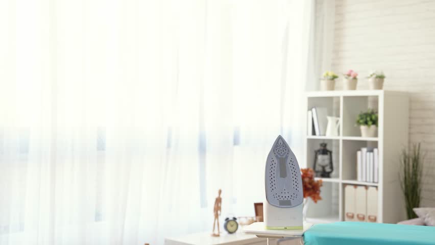 attractive housewife holding clean clothing in laundry basket and walk into the living room with smile ready to doing housekeeping with ironing board.