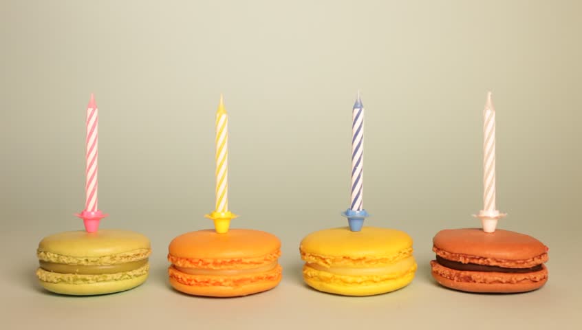 Macarons with candles arranged horizontally on a beige background.