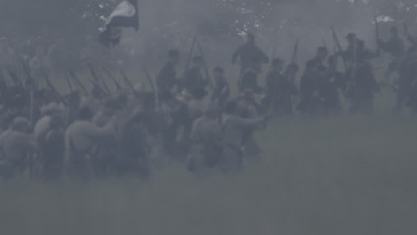 VIRGINIA - MAY 2017 - large-scale, epic Civil War anniversary reenactment -- in the middle of battle. Confederate soldiers march into battle against Union Army, across tall grass field, fire muskets.