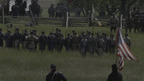 VIRGINIA - MAY 2017 - large-scale, epic Civil War anniversary reenactment -- in the middle of battle. Confederate soldiers march into battle against Union Army, across tall grass field, fire muskets.