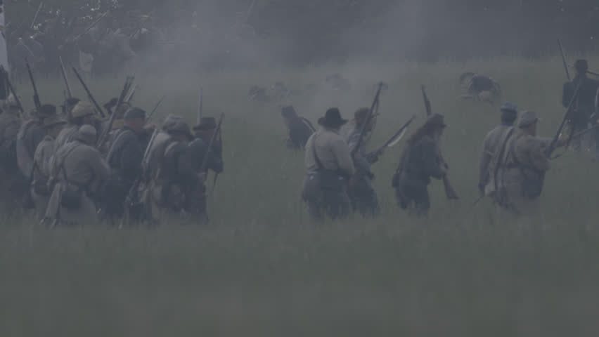 VIRGINIA - MAY 2017 - large-scale, epic Civil War anniversary reenactment -- in the middle of battle. Confederate soldiers march into battle against Union Army, across tall grass field, fire muskets.
